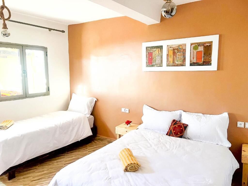 Una habitación de hotel con dos camas individuales, piso de madera, una ventana y tres cuadros enmarcados en la pared.