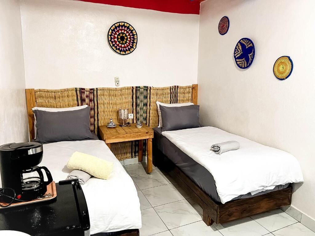A room with two beds, a coffee maker, and a small table with a lamp.