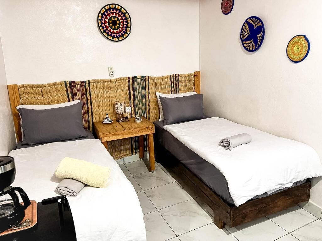 Una habitación con dos camas, una cafetera, una mesita y placas decorativas en la pared.