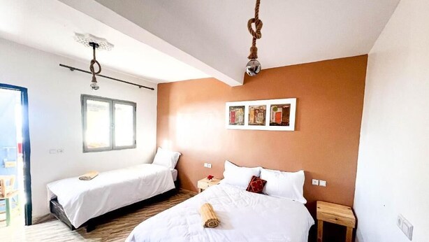 A hotel room with two beds, a wooden floor, a ceiling light fixture, and a window. - Superbo Stay (Taghazout)