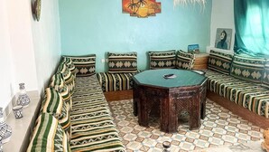A room with a sofa set, a round wooden table, and a wall-mounted painting. - Superbo Stay (Taghazout)
