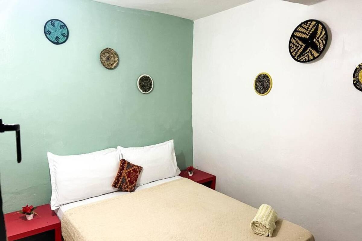 Un dormitorio con cama, almohadas, una mesita de noche roja, una lámpara roja y adornos en la pared.