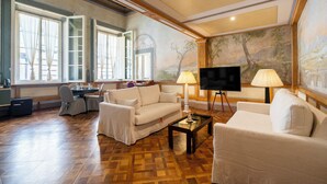 A spacious living room with a large flat-screen TV, two lamps, a sofa, a coffee table, and a dining area with a table and chairs.