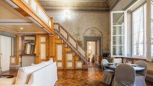 A spacious room with a wooden staircase, a dining area with round tables, and a large window.
