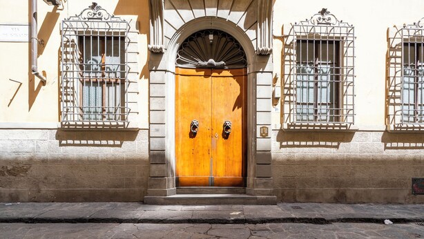 A building with a large wooden door, two windows with metal grilles, and a stone-paved street.