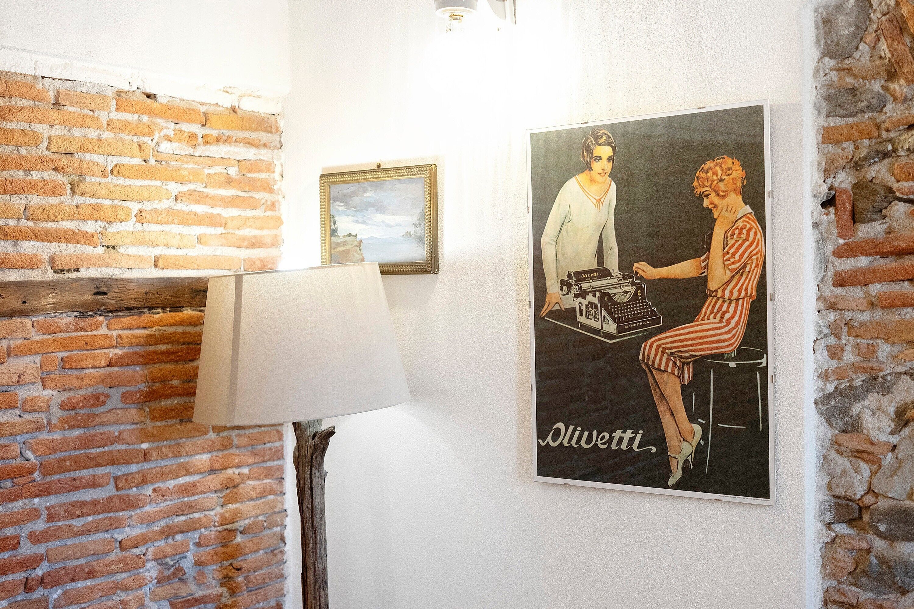 Una stanza con una parete in mattoni, un quadro incorniciato, un poster e una lampada.