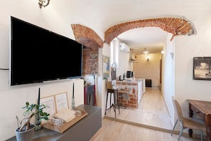A modern living space with a flat-screen TV, a potted plant, and a dining area with a brick archway. - Holiday Home 'La Volta Segreta' with Mountain View, Wi-Fi and Air Conditioning (Albenga)
