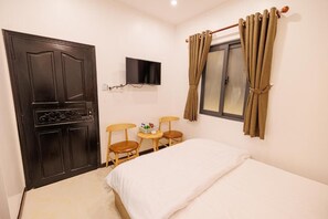 A bedroom with a bed, a TV mounted on the wall, a window with curtains, and a door. - Happy Hotel (Bac Lieu)