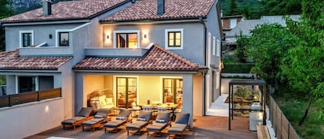 A two-story house with a swimming pool, outdoor seating, and a view of mountains.