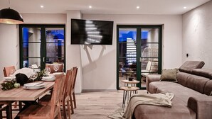 Een moderne woonkamer met een eethoek, een flatscreen televisie aan de muur en een groot raam met uitzicht.