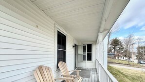 A porch with two Adirondack chairs, a white railing, and a view of a street with houses and cars. - Downtown Brunswick 1st FL Sun Drenched With Porch (Brunswick)