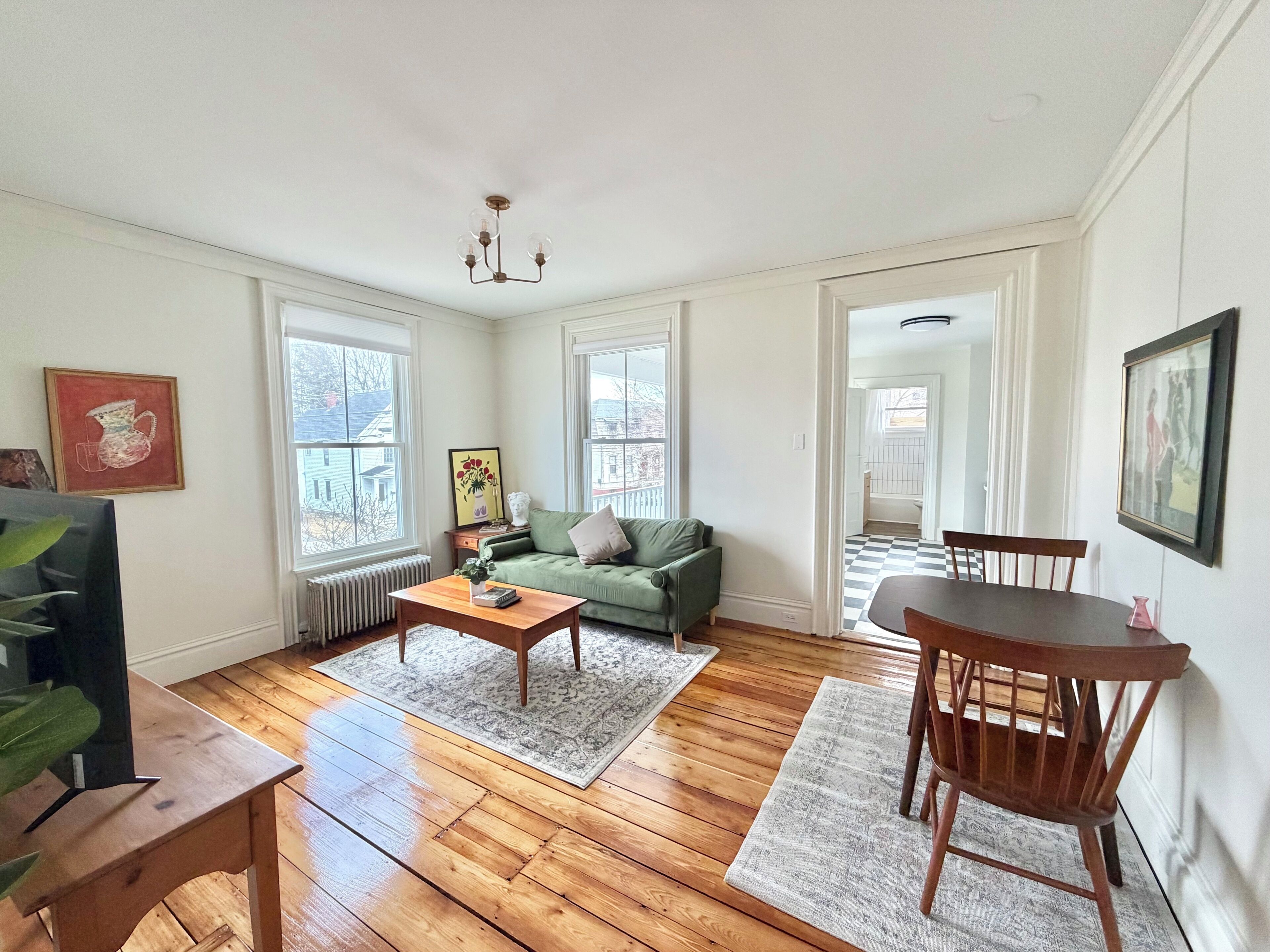 A spacious living room with hardwood flooring, a green sofa, a wooden coffee table, and a dining area with a wooden table and chairs.