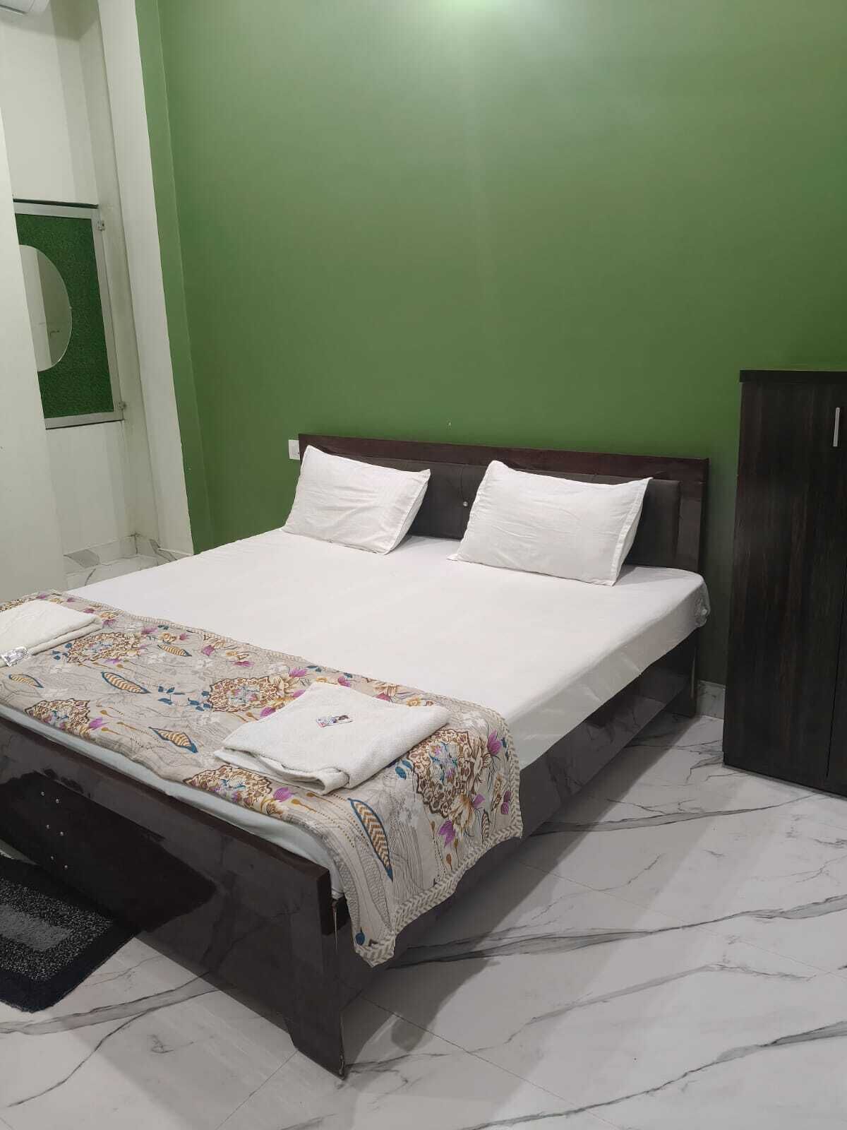 A bed with a floral bedspread and two pillows, a dark wooden headboard, and a green wall.