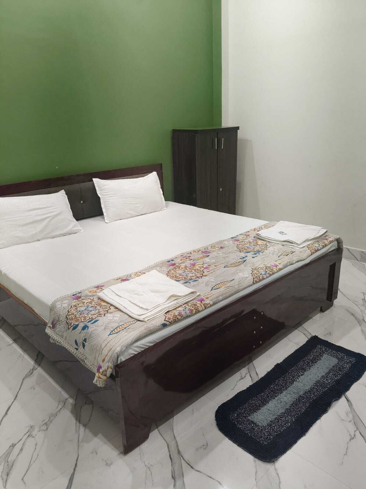 A bed with a floral bedspread and pillows, a dark wooden headboard, a green wall, a wardrobe, and a marble floor.