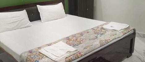 A bed with a floral bedspread and pillows, a dark wooden headboard, a green wall, a wardrobe, and a marble floor.