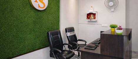 A modern office with a green wall, two black office chairs, a wooden desk, a small shrine, and a wall-mounted fan.