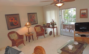 A living room with a ceiling fan, a television, and a glass coffee table. - Alii Villas 219 - Close to town (Kailua Kona)