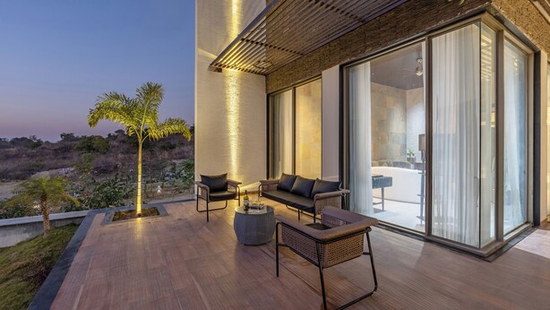 Un espacio moderno al aire libre con sofá, sillones y una mesa de centro, con vistas a un jardín ajardinado.