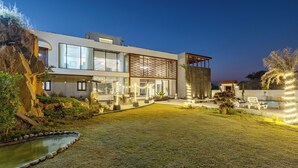 Una casa moderna con fachada de vidrio amplia, piscina y mobiliario para exteriores.