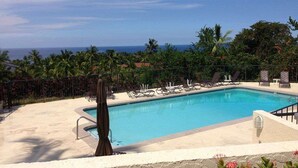 Piscina com espreguiçadeiras e vista para o oceano.
