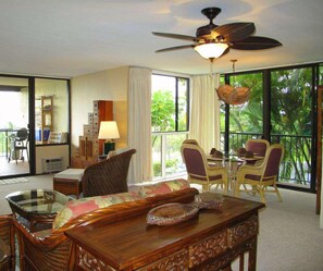 A room with a dining table, chairs, a ceiling fan, and large windows. - Country Club Villas - Ocean View Condo • Golf Course • Walk to Bay (Kailua Kona)