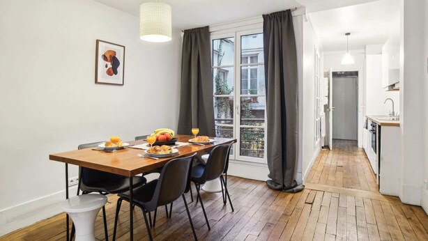 Een eethoek met een houten tafel, zwarte stoelen en een hangende lamp.