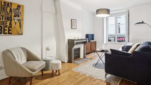 Een woonkamer met een bank, fauteuil, open haard en een groot raam.