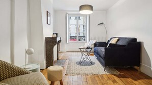 Een moderne woonkamer met een donkerblauwe bank, een klein rond tafeltje, een vloerlamp en een kamerbreed tapijt met een patroon.