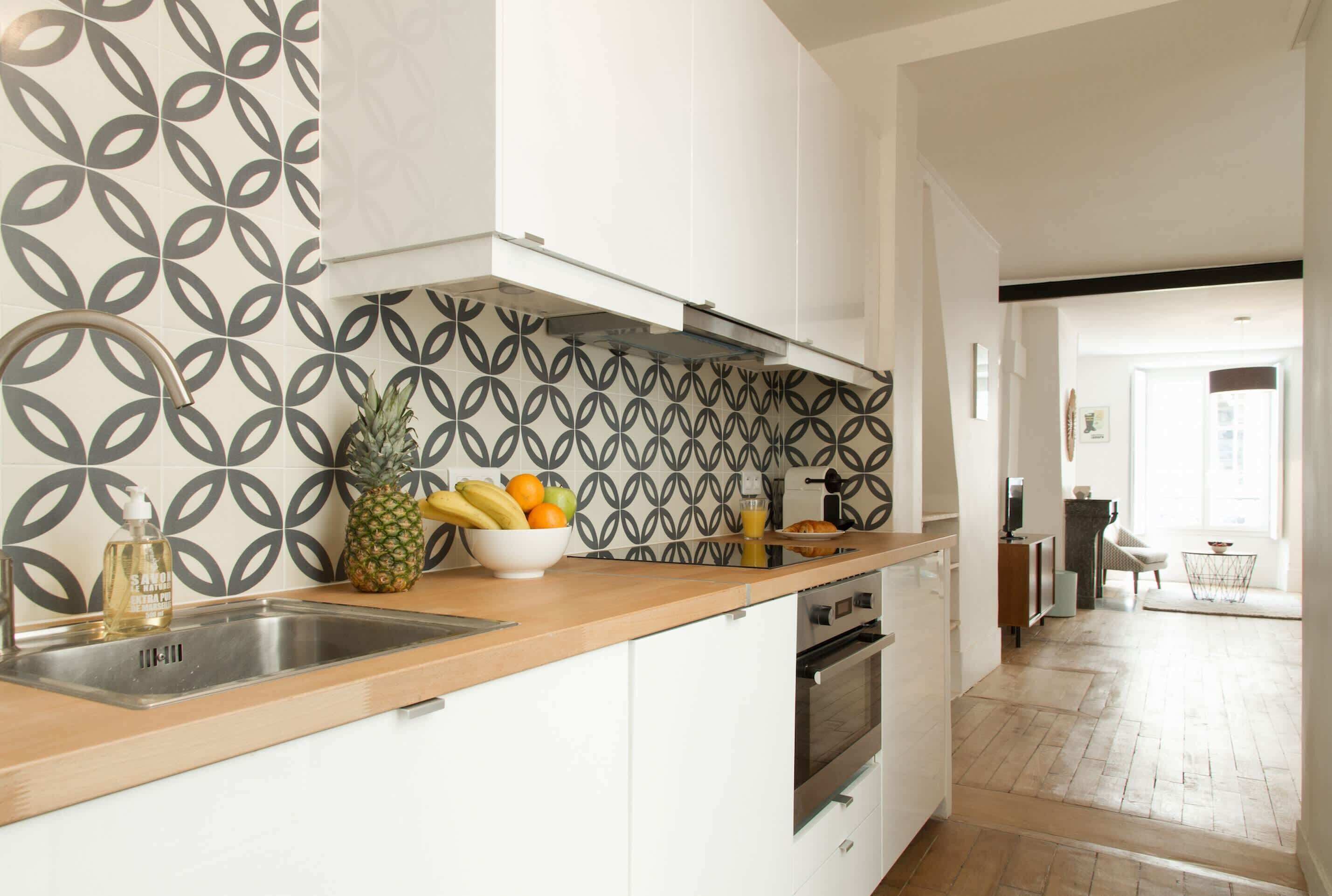 Een keuken met een decoratieve spatwand, een houten aanrechtblad en een schaal met fruit.