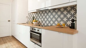 Een moderne keuken met witte kasten, een houten aanrechtblad, een inbouwoven en een achterwand met een patroon.