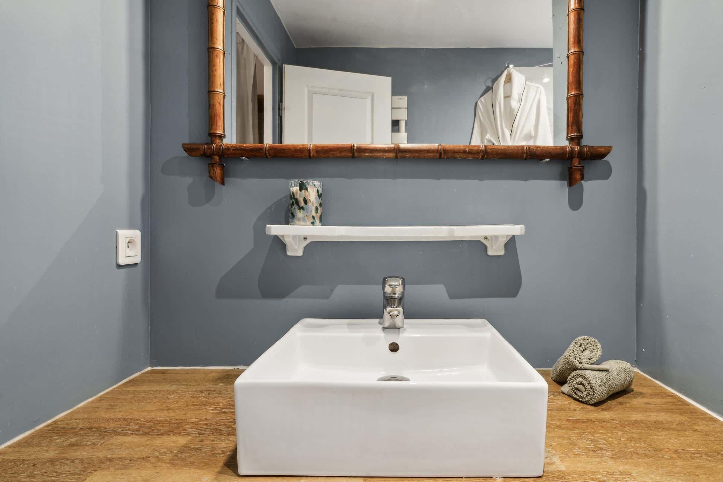 A bathroom with a white sink, a mirror with a bamboo frame, and a towel rack with towels.