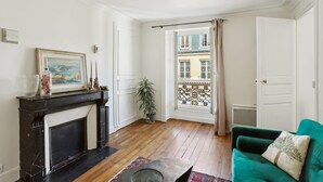 Una sala de estar con chimenea, un sofá verde, una planta en maceta y vistas al balcón exterior.