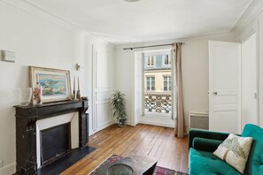 Ein Wohnzimmer mit Kamin, einem grünen Sofa, einer Topfpflanze und Blick auf den Balkon.