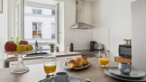 Una cocina moderna con comedor, mostrando un desayuno con cruasanes, fruta y jugo de naranja.
