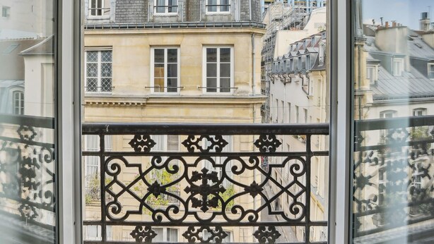 Un balcón con barandilla de hierro forjado, con vista a una hilera de edificios históricos de varios pisos y diferentes estilos arquitectónicos.