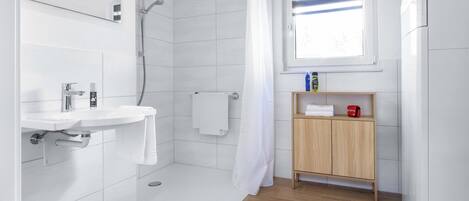A modern bathroom with a shower, a sink, a wooden cabinet, and a window.