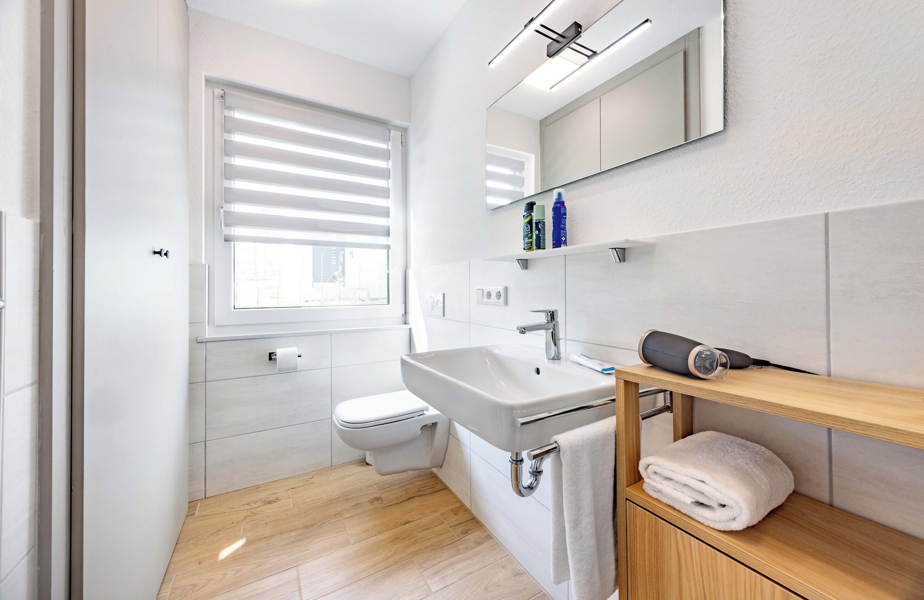 Une salle de bain moderne équipée de toilettes, d’un lavabo et d’une fenêtre avec stores.