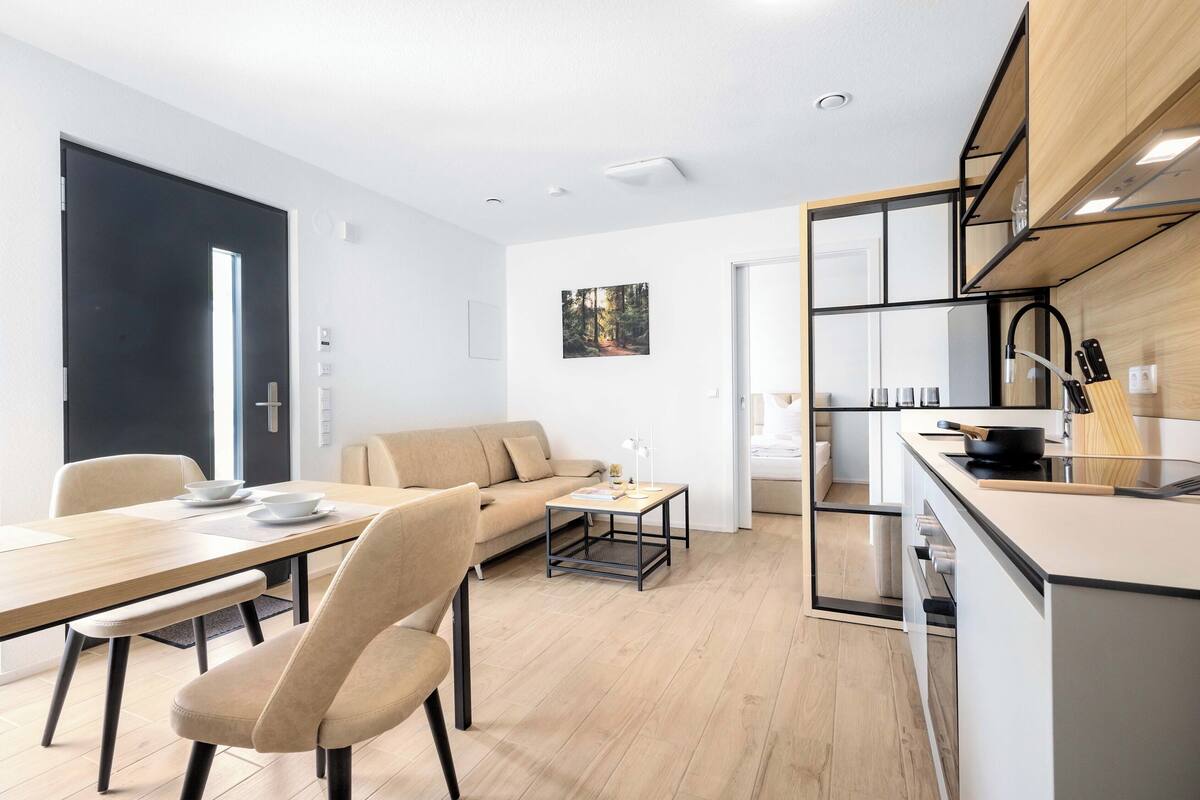 A modern living space with a dining area, a sofa, a coffee table, and a kitchen area with a stove and utensils.