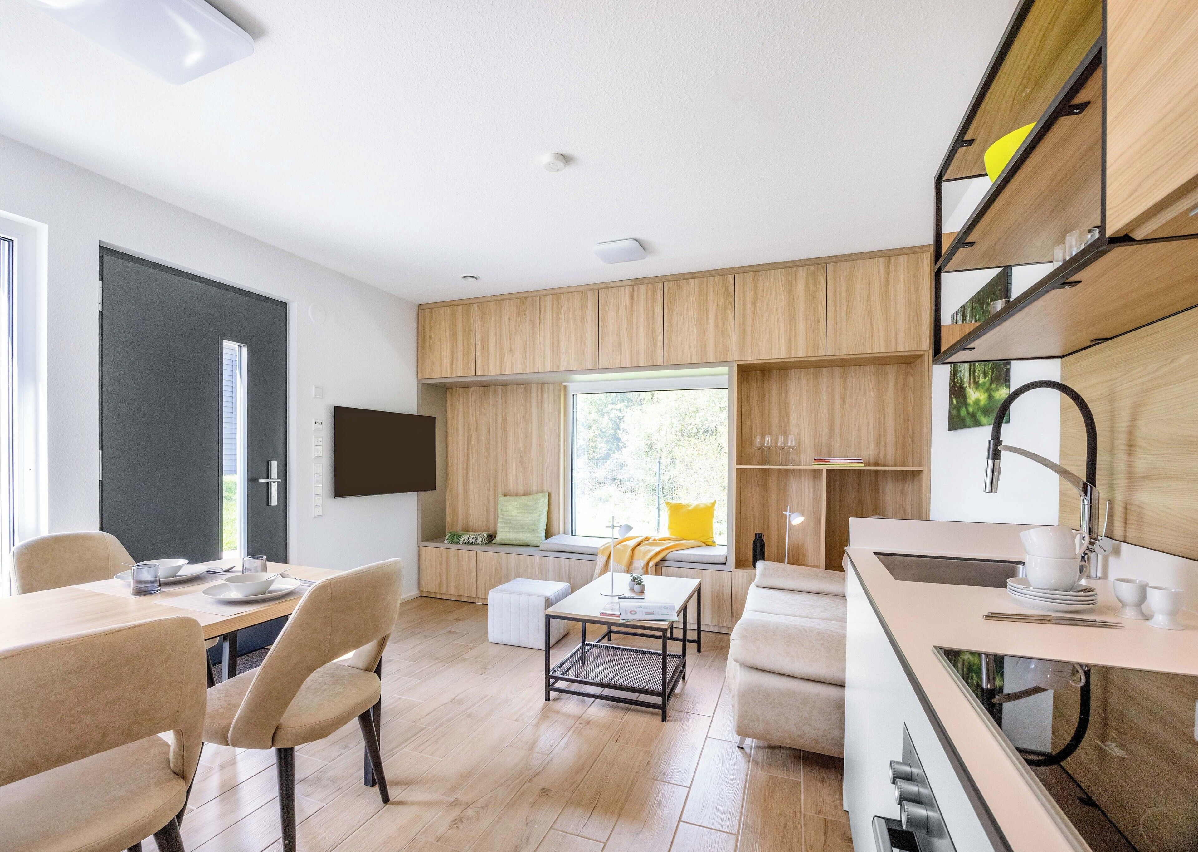 A modern kitchen with built-in appliances, a dining area with a table and chairs, and a seating area with a sofa and a window.