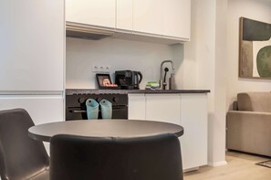 A modern kitchen with white cabinets, a black countertop, a coffee machine, and a dishwasher. There is a round table with two chairs and a sofa in the background. - TYS One Bedroom Basement Apartment (Reykjavík)