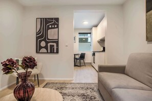 A living room with a sofa, a coffee table, a vase with flowers, a rug, and a painting on the wall. - TYS One Bedroom Basement Apartment (Reykjavík)