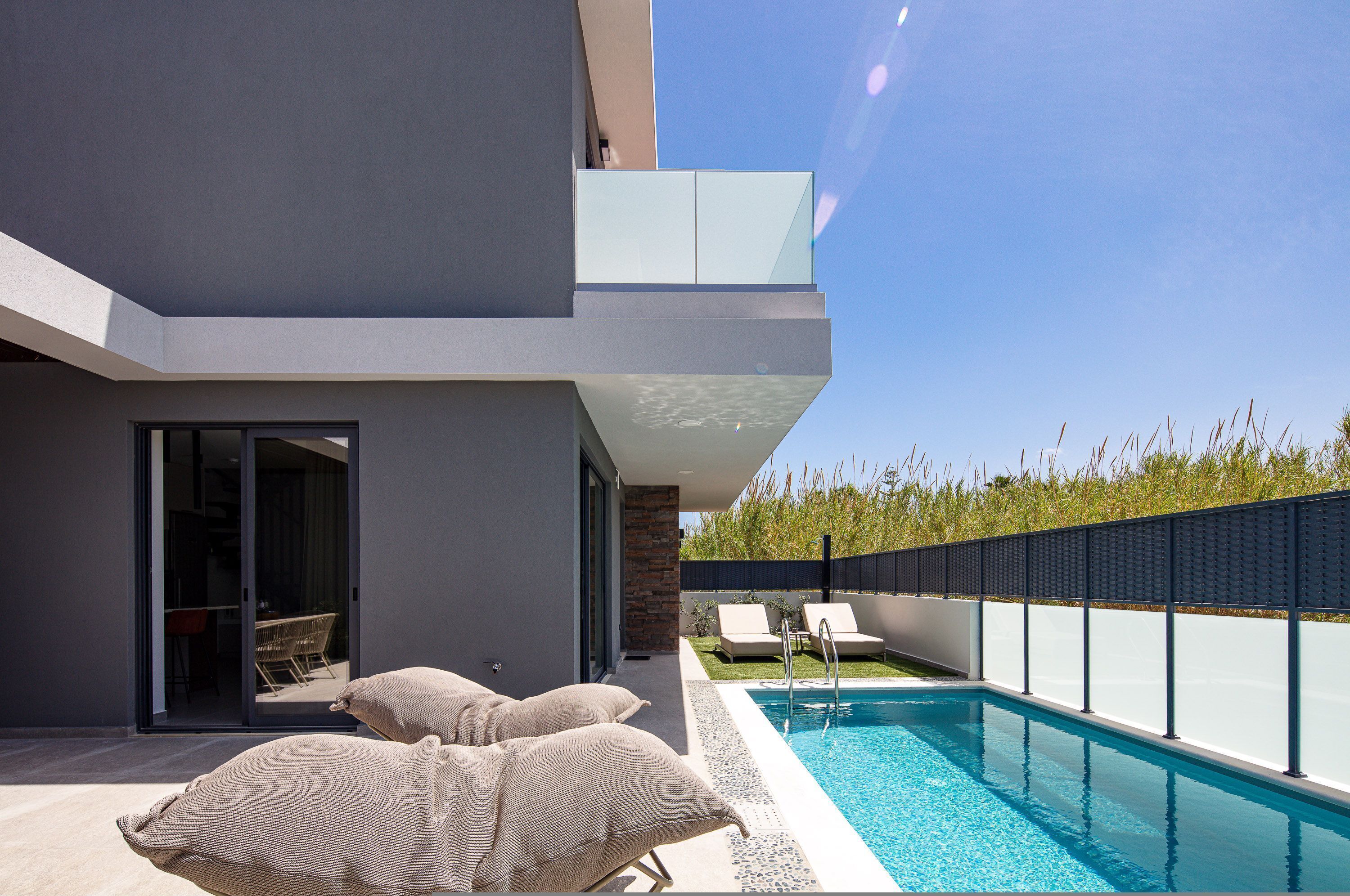 A modern outdoor pool area with a clear blue sky, a pool, and lounge chairs.