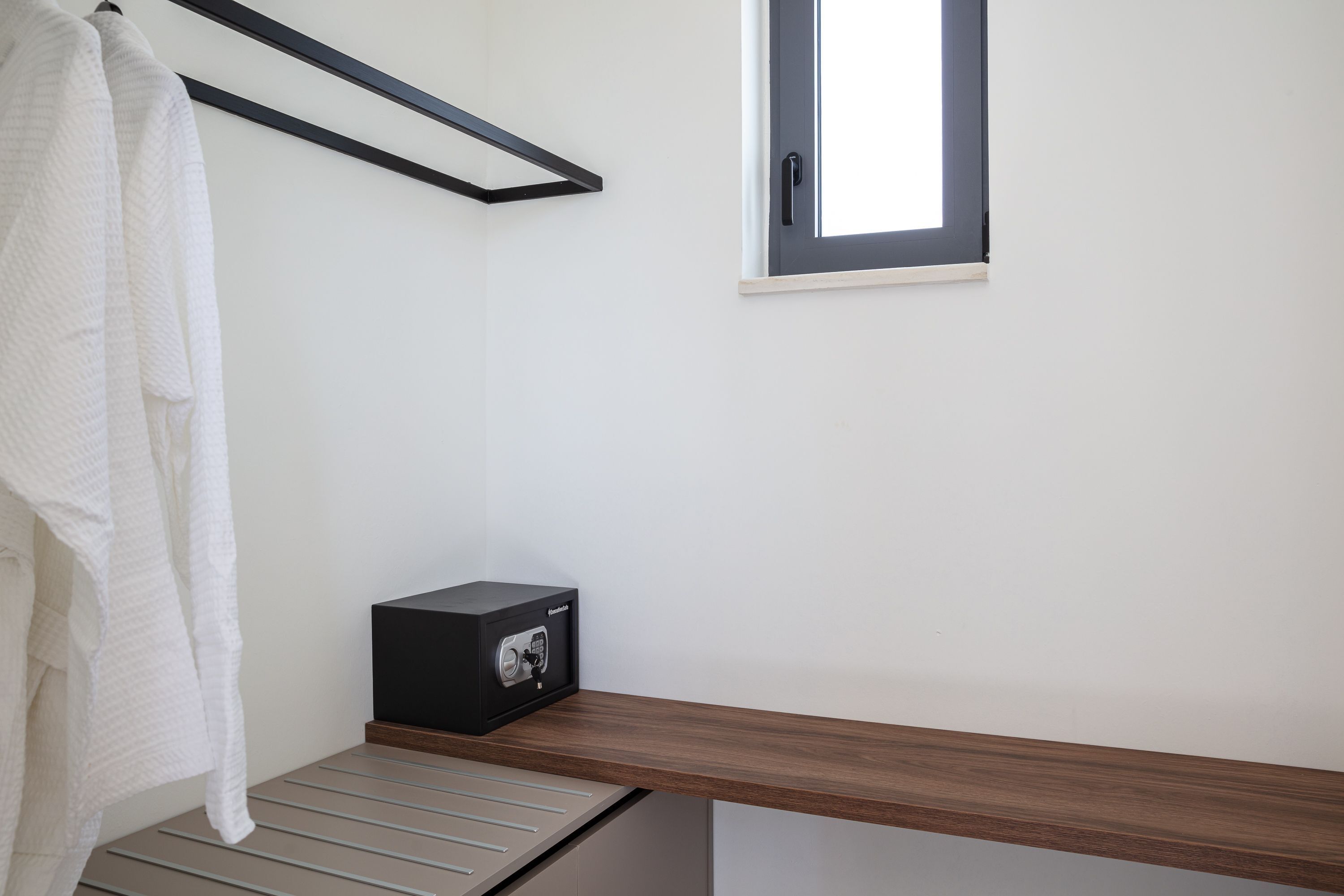 Une salle de bain équipée d’un porte-serviettes, d’une fenêtre, d’une étagère en bois et d’un coffre-fort noir.