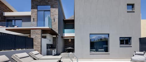 Un edificio moderno con piscina, sillas de descanso y zona de comedor.