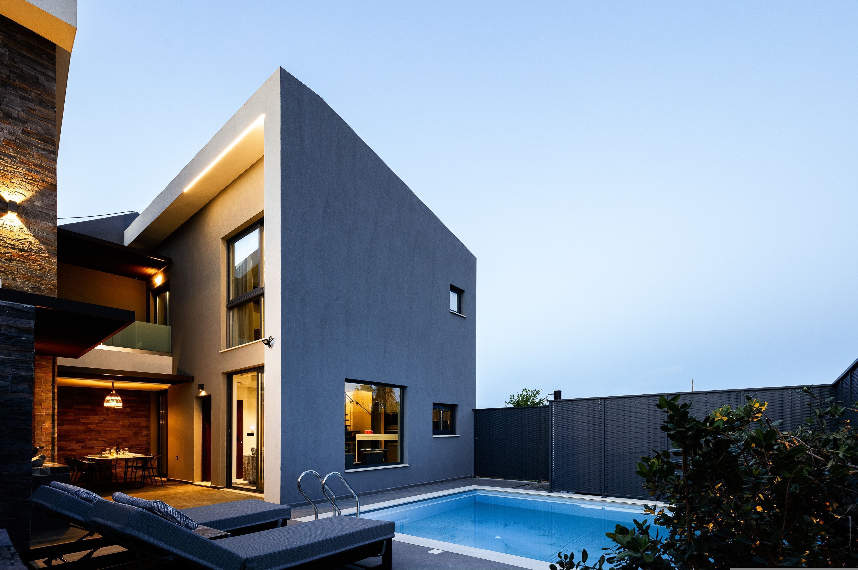 A modern house with a pool, a dining area, and a lounge with a view of the pool.