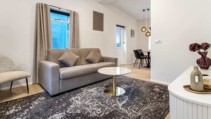 A modern living room with a grey sofa, a round coffee table, a patterned rug, and a dining area with a table and chairs. - TYS One Bedroom Apartments (Reykjavík)