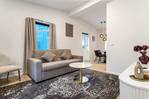 Ein modernes Wohnzimmer mit grauem Sofa, rundem Couchtisch, einem gemusterten Teppich und einem Essbereich mit Tisch und Stühlen.