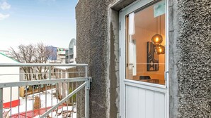 A building with a textured exterior, a balcony with a metal railing, and a window with a hanging light fixture. - TYS One Bedroom Apartments (Reykjavík)