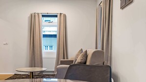 A room with a sofa, a small round table, a window with curtains, and a radiator. - TYS One Bedroom Apartments (Reykjavík)