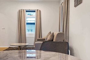 Ein Zimmer mit einer Couch, einem kleinen runden Tisch, einem Fenster mit Vorhängen und einer Heizung.